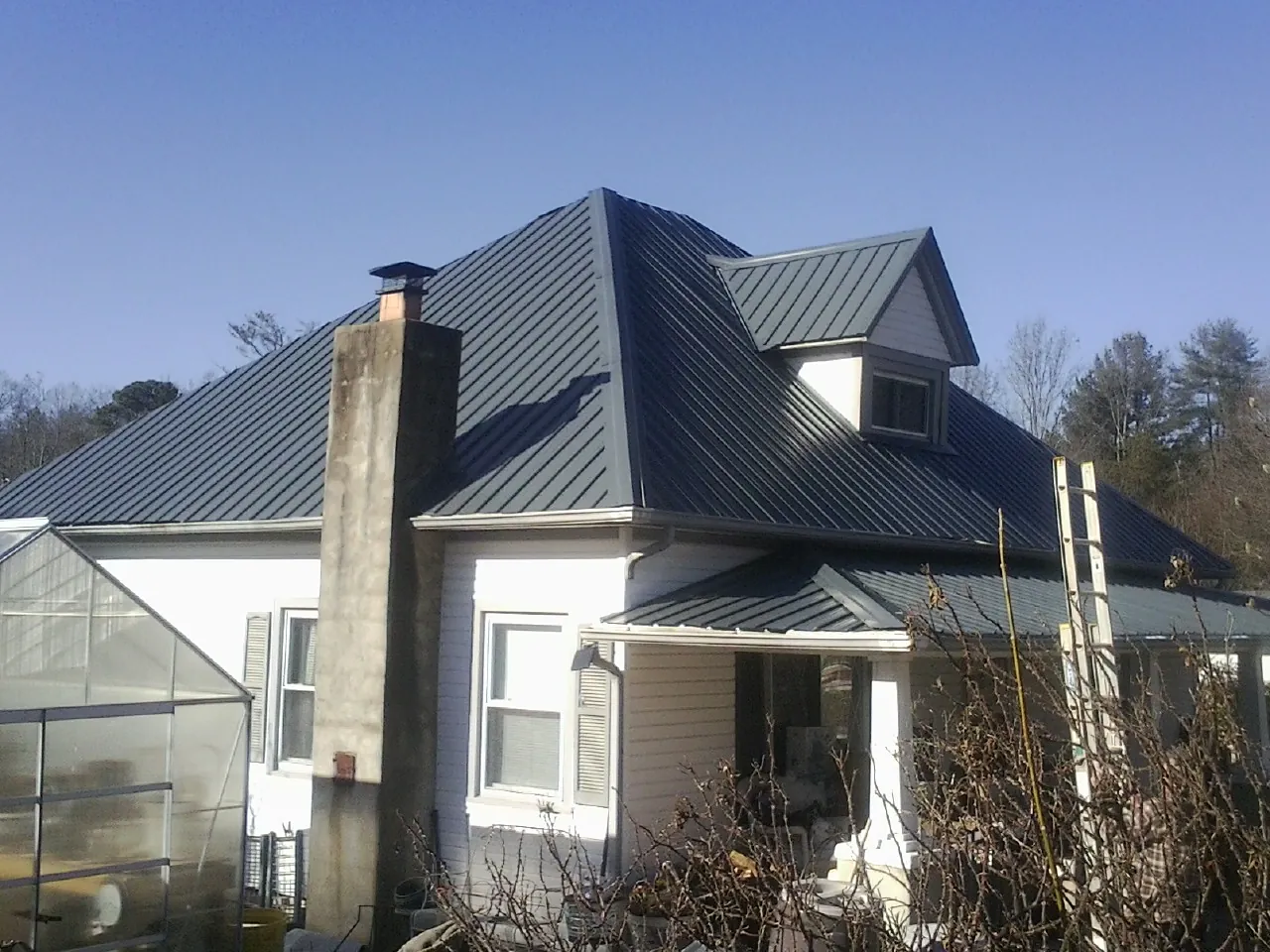 Dark blue standing seam metal roof on a white farmhouse with dormer — Slate & Tile Roof Repair by Roofing Brothers in Beverly Hills