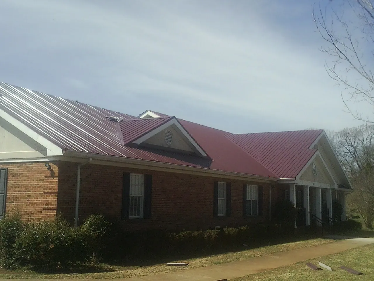 Red metal roof with gabled entries on a long brick building, from a Hail Damage Roof Repair job in Beverly Hills