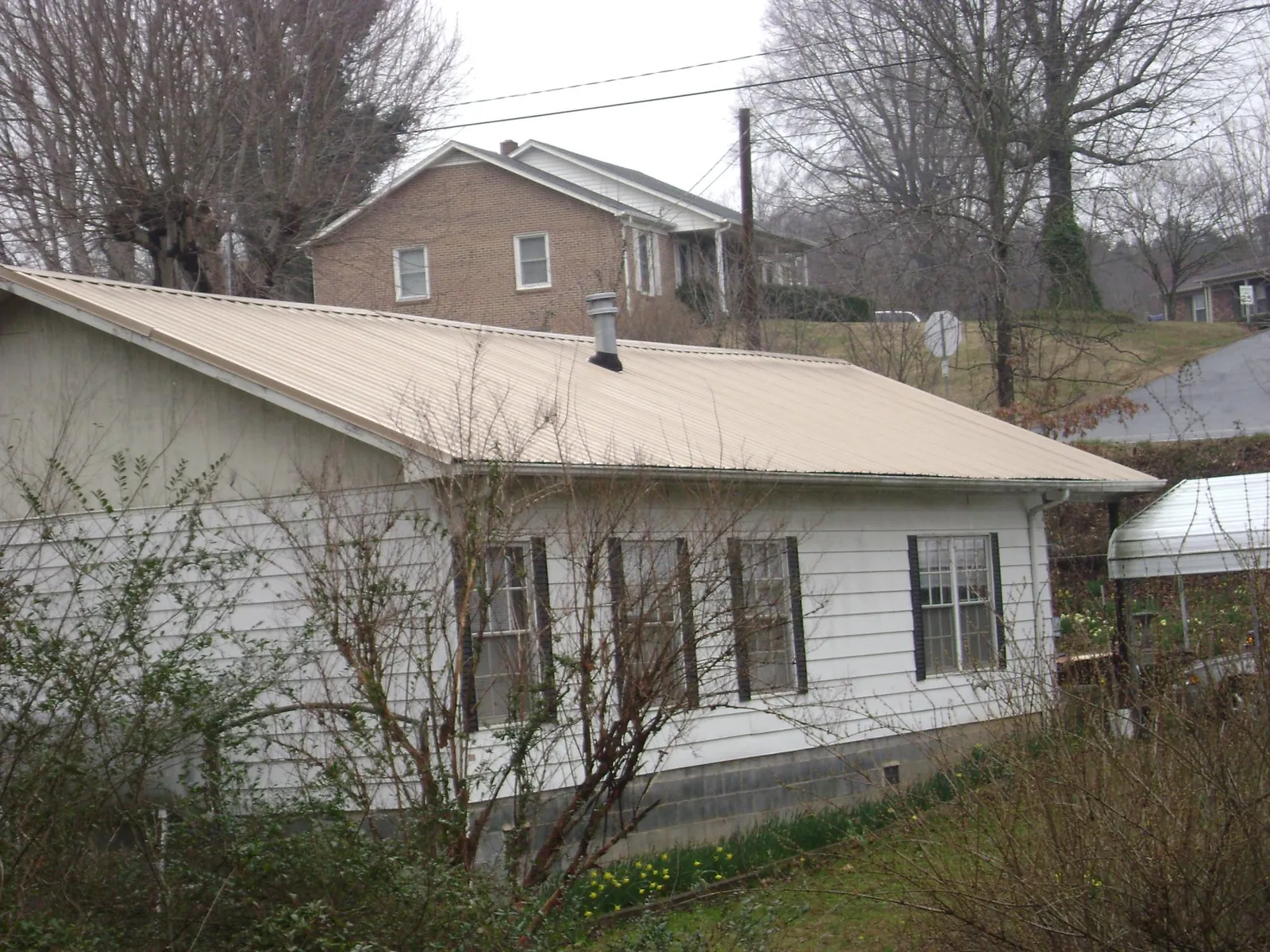 Tan metal roof on a white sided house set into a hillside — Commercial Roofing by Roofing Brothers in Beverly Hills
